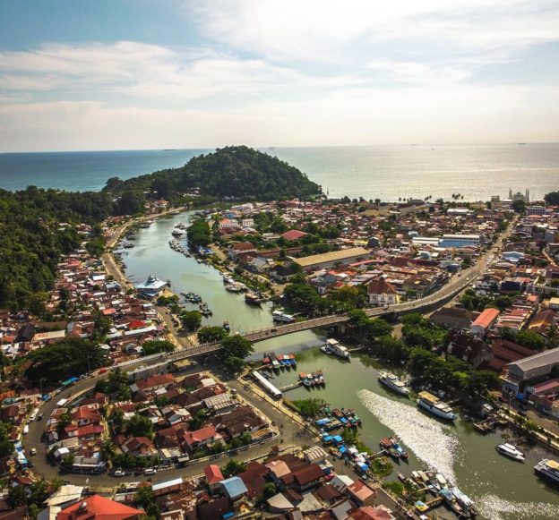 Pemandangan indah Jembatan Siti Nurbaya di Padang saat matahari terbenam, dengan latar belakang Sungai Batang Arau dan kapal-kapal nelayan